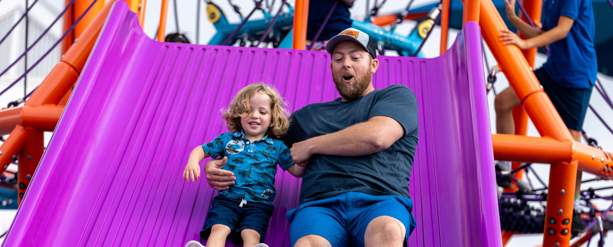 A dad and young son sliding down a Mighty Descent slide together